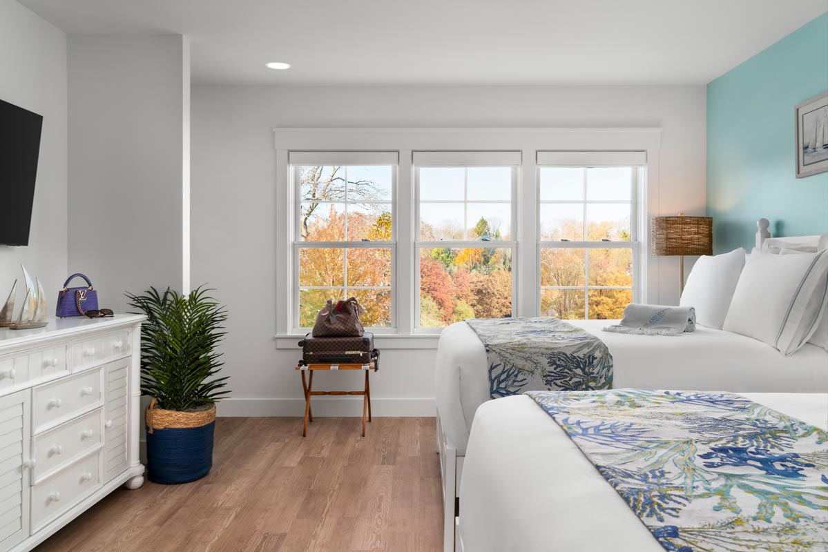 Bedroom with two beds dressed with white linens, with a Louis Vutton suite case next to it and a TV with stand with a purse sitting on top