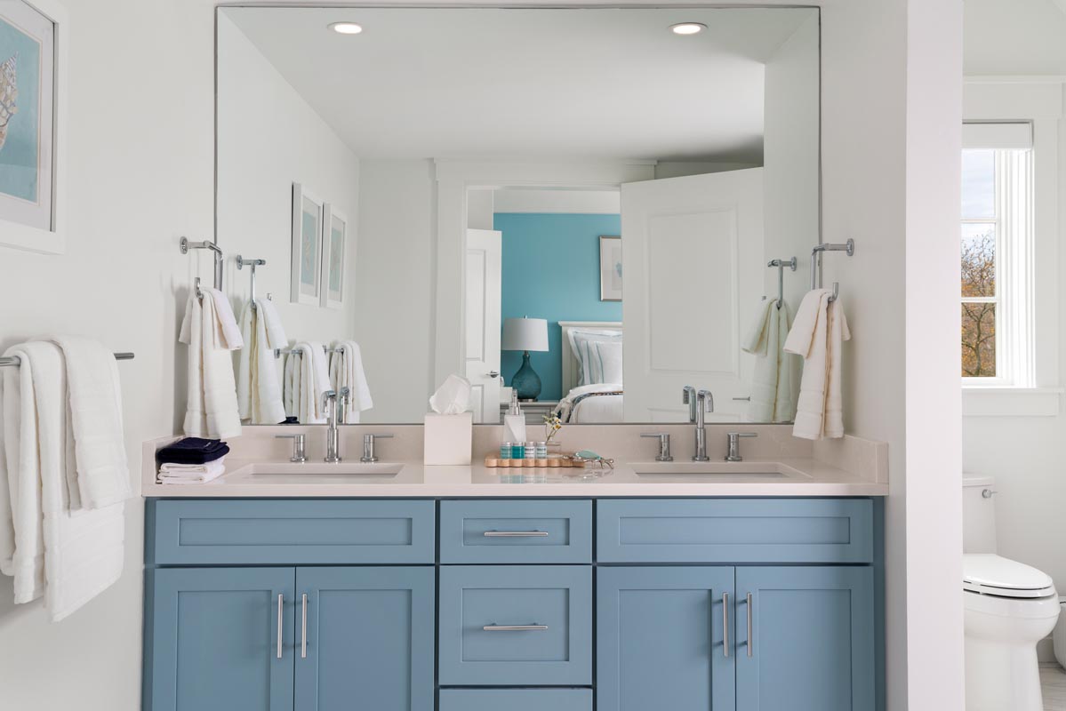 Bathroom vanity with sink and mirror showing bed in the background