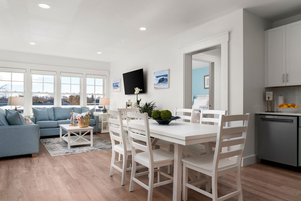 Open kitchen with a dining table next to a cozy living area with sofas, leading to a bedroom through a welcoming entryway.