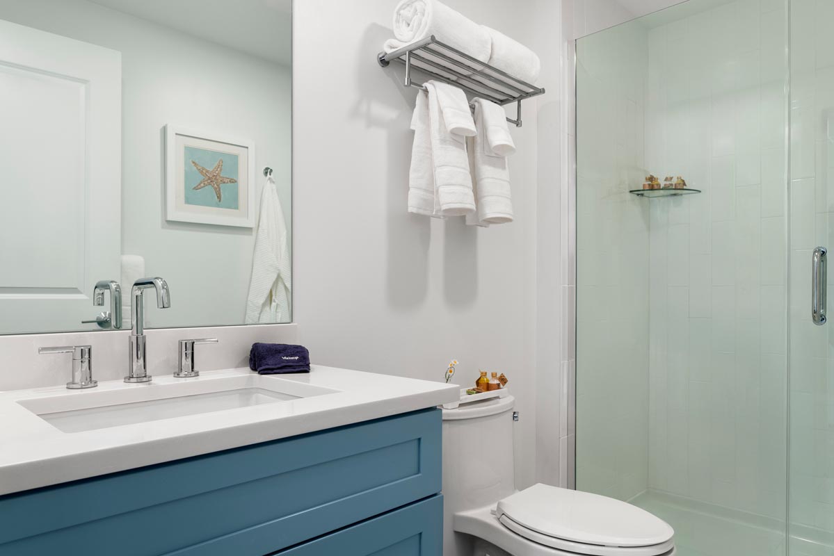 Bathroom with sink, mirror, toilet with towels hanging above it next to a glass shower