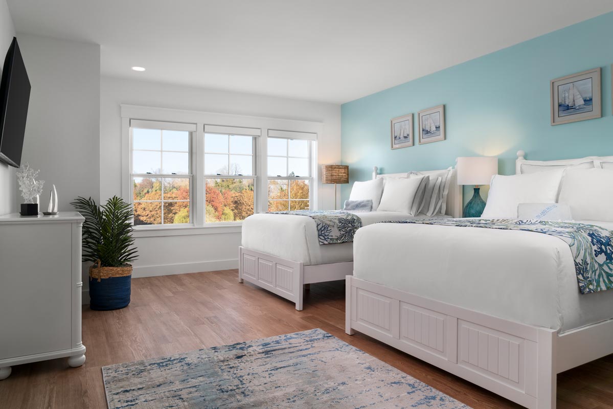 Bedroom with two beds dressed with white linens next to it and a TV with stand