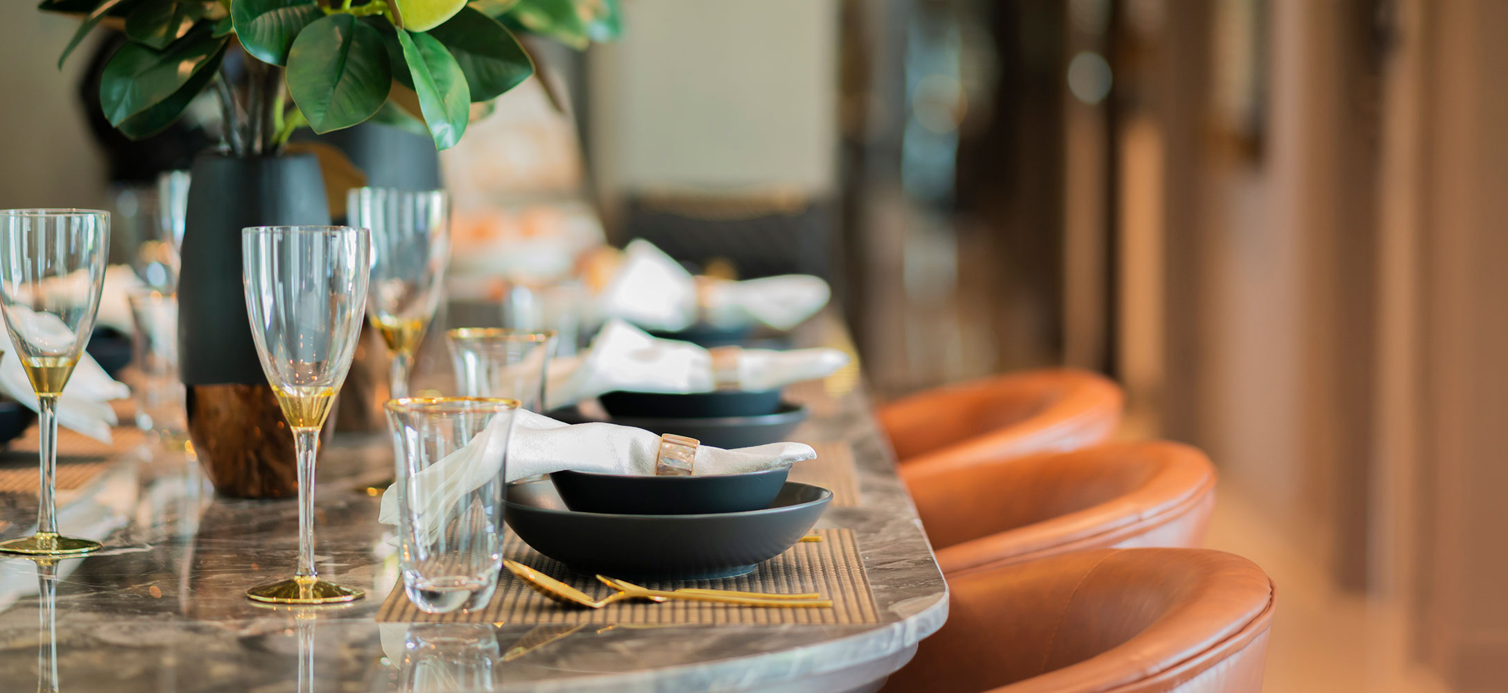 Dining table with leather seats and plates, bowls, cutlery and wine glasses