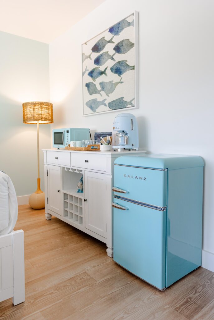 Room with a bed, dresser with Smeg coffee maker and mugs on top and piece art on the wall of fish